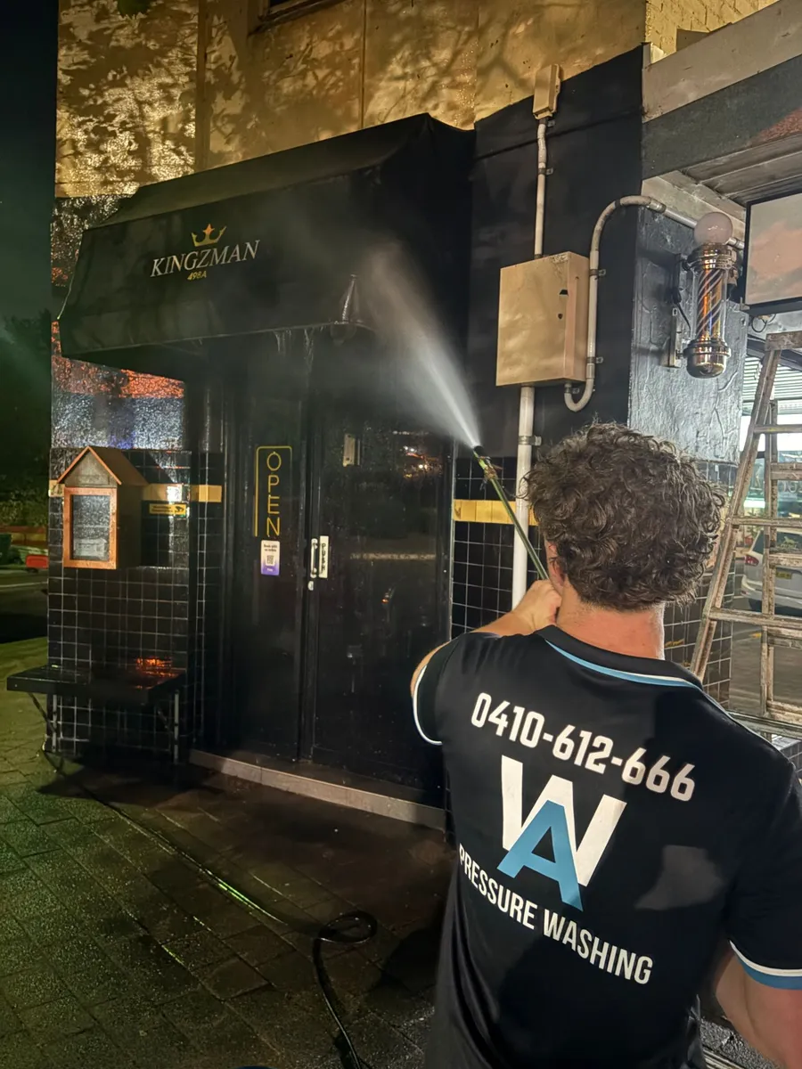 Alfie from AW Pressure Washing soft washing a black shopfront awning and tiled entry at night