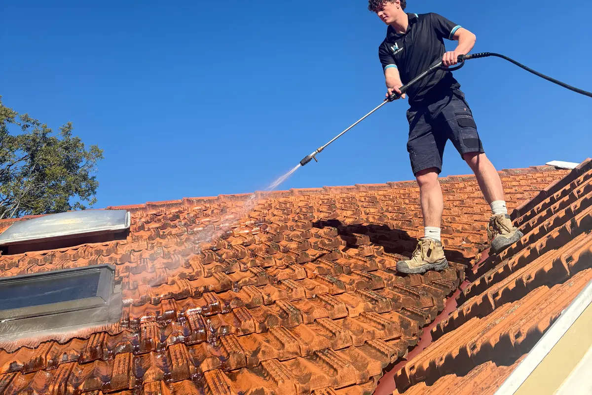 AW technician pressure washing a terracotta tile roof